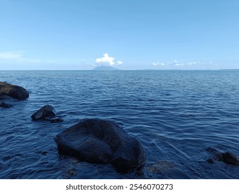 View of Malalayang Beach Dive Point Manado, with ketapang trees, rocky beach and the backdrop of the old Manado island seen in the distance, with the sea and blue sky with thin clouds - Powered by Shutterstock