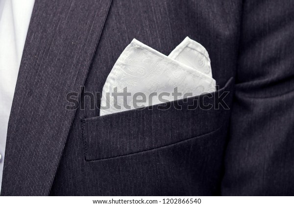 View to the male coat pocket with a fixed white\
square. Men\'s suit accessories. Wedding male guest\'s attire. Male\
wedding style. Formal dinner outfit for men. Elements of a suit.\
Pocket square folding