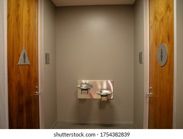 View Of Male And Female Bathroom Doors Across From Each Other And Drinking Water Fountain Mounted On The Wall.