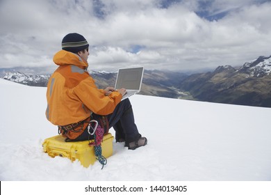 View of a male hiker using laptop on snowy mountain landscape