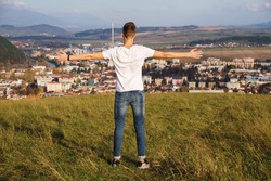 A View Of A Male Standing On A Hill With His Arms Open While Proudly Looking At His Hometown