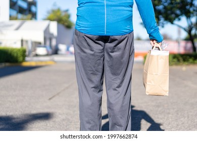 View of a man from behind walking down the street carrying a paper recyclable shopping bag full of groceries purchased from the local coffee shop