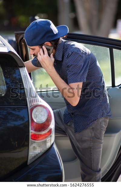 A view\
of a man entering a ride share vehicle from the back right side\
back seat, meanwhile talking on cell\
phone.