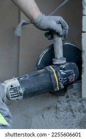 View of a man hands holding and using an angle grinder with diamond disk to cut a hole in the house wall. Close up view.