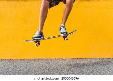 View of man on shorts legs jumping with skateboard on yellow background. - Powered by Shutterstock