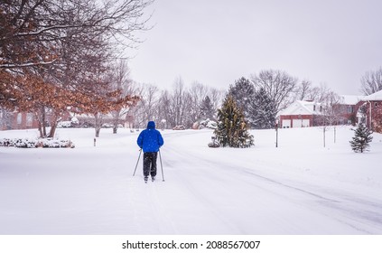 View Of Man Skiing  In Suburban Neighborhood After Snowfall; Houses In Background; Winter In Midwest