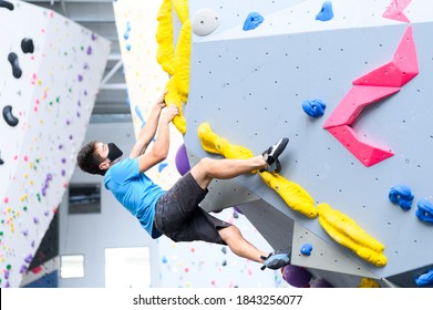 view of a man wearing a COVID-19 pandemic mask climbs a bouldering wall in a climbing gym following social distance guidelines for exercise - Powered by Shutterstock