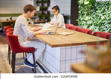 View Of Man And Woman Sitting With Laptops And Papers At Table In Cafeteria Having Big Load Of Work