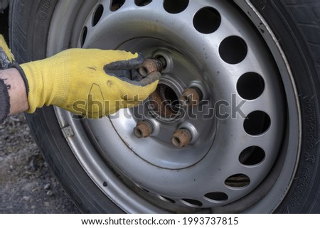 View of mans hands in yellow gloves screwing out wheel bolts.