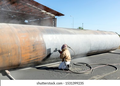 View of the manuel sandblasting to the large pipe. Abrasive blasting more commonly known as sandblasting is the operation of forcibly propelling a stream of abrasive material against a surface.
