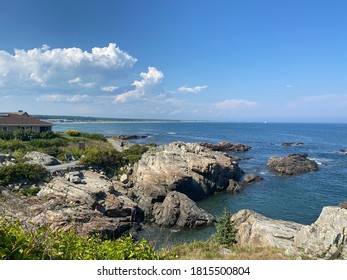 The view from Marginal Pathway in Ogunquit Maine. Large rock cliffs and ocean as far as you can see. A few clouds in the sky and a house to the left.