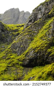 A View Of Massive Black Rocks Covered With Fresh Green Moss On A Spring Or Summer Day