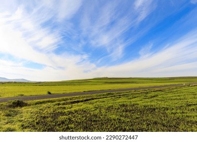 view of meadows and hills against the blue sky with clouds