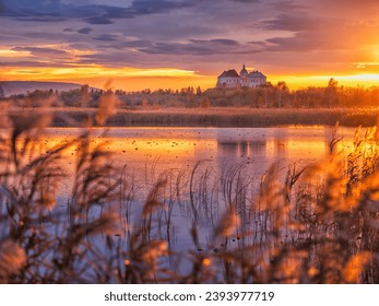 view to medieval castle through reeds and lake in golden hour with golden light of sun under clouds with free space