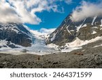 View of melting Steindalen glacier in northern Norway. Turquoise-colored ice in cracks. Calm meltwater collecting in a lake between moraine and glacier. People walking towards the glacier in distance