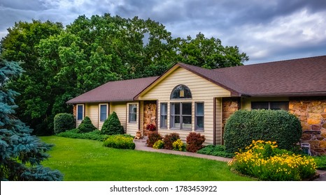 View Of Midwestern Suburban House With Dark Sky In Background And Landscaped Front Yard In Foreground; Summer In Midwest