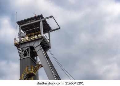 View of the mine shaft elevator wheels against the cloudy sky. The object is lit by natural sunlight passing through the clouds