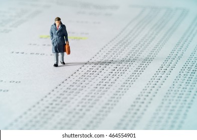View of miniature toy, businessman walking on financial documents. Soft blue filter.