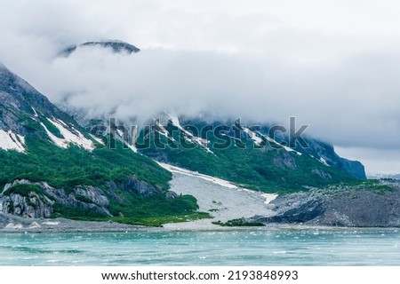 A view mist decending on the rocky, verdant shoreline close to the Margerie Glacier in Glacier Bay, Alaska in summertime