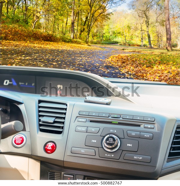 view of modern car dashboard with\
start power engine button and keys, fall road in\
background