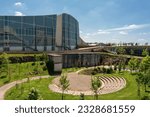 view of a modern office building with glass windows on its facade next to a park full of trees and grass with an amphitheatre 