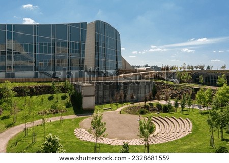 view of a modern office building with glass windows on its facade next to a park full of trees and grass with an amphitheatre 