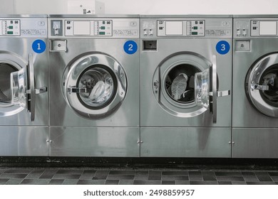 View of a modern stainless steel machines in a laundromat or laundrette. Public laundry with multiople washing machines. Frontal view, one door open - Powered by Shutterstock