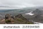 View from the mountain to the Kamchatka valley. The bizarre outlines of the top, sparse vegetation on stony soil. In the distance, in the fog, you can see paths, melted snow. Cloudy sky. Mount Camel
