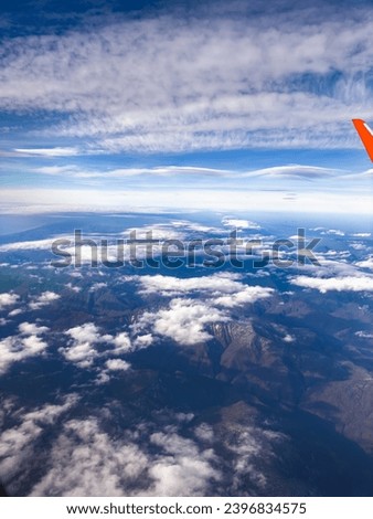 view of the mountains from the height of a flying airplane, clouds, mountains, airplane wing, blue sky, dawn.
