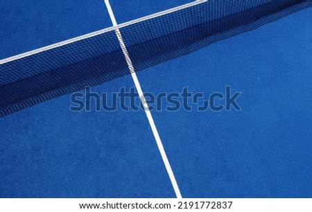 View of the net and the centre line of a blue paddle tennis court. Racket sports