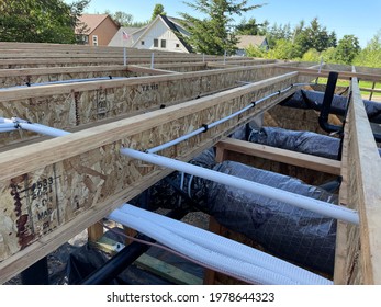 View Of New Installation Of Ventilation Ductwork And Plumbing Pipes Under The Open Floor Trusses Of A New Home Construction Project