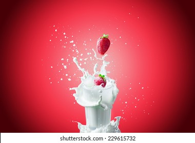 Vue d'une belle fraise rouge fraîche tombant dans le lait en verre faisant une grande éclaboussure sur fond rouge : photo de stock