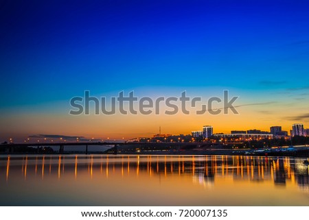View of the night city from the river bank. Bridge leading to the city on a sunset background. Welcome to UFA, Russia.