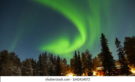 View Of The Northern Lights With Trees And Cottages