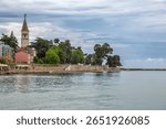 View of Novigrad historic old town peninsula from Adriatic Sea showing iconic bell tower, medieval stone buildings, and ancient walls under blue sky in Croatia.