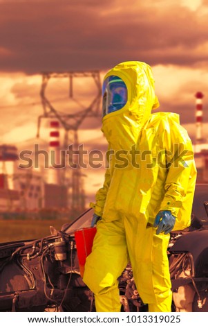 View of nuclear power plant and firefighter in a chemical protective hazmat
suit next the demaged car.