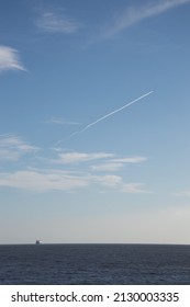 View of the ocean with a boat and contrail on a blue cloudy sky. 