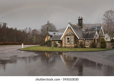 View Of An Old House By The Road Under A Rainbow Arch On A Rainy Day In Crieff, Perth And Kinross, Scotland, UK, With Its Reflection On A Puddle On The Foreground.