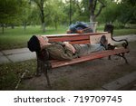 View of old man lying on bench in city park. Homeless man relxing sleeping on bench.