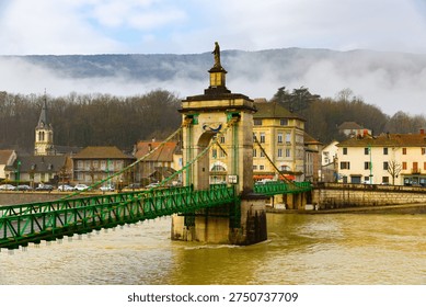 View of old suspension bridge with statue of Virgin Mary across Rhone river and embankment of Seyssel on winter day, Ain department, France