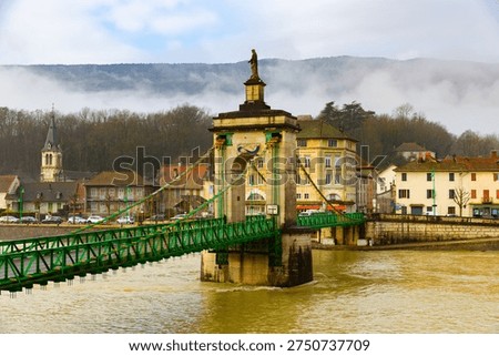 View of old suspension bridge with statue of Virgin Mary across Rhone river and embankment of Seyssel on winter day, Ain department, France