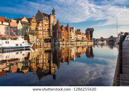 View of old town Gdansk (Gdańsk), Poland (Polska) with merchants' house, Mariacka Gate, and famous historic Medieval Crane. Beautiful morning on the Motlava River. No wind, no people, only one angler.