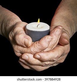 View Of The Old Woman Hands Holding A Burning Candle On A Black Background