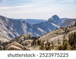 View from Olmsted Point in Yosemite National Park showcasing the majestic granite peaks, including Half Dome, with a rugged forest below and clear skies above.