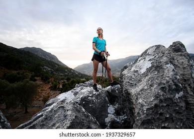 view on beautiful woman tourist with trekking poles standing on large stone against sky in mountains in Turkey - Powered by Shutterstock