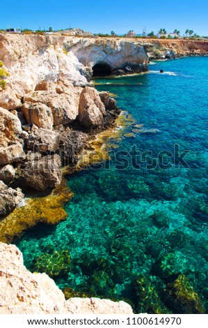 View on a cave near Agia Napa, Cyprus, majestic natural landmark. Yellow brown high stone cliffs near transparent amazing blue water. Warm cloudless day. Feeling of wanderlust