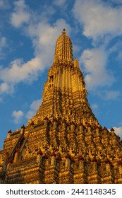 View on Central prang of Wat Arun buddhist temple against blue sky in the rays of the yellow sunset at Bangkok, Thailand. Central prang can be considered as a pagoda or stupa. Temple of Dawn
