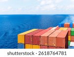 View on the containers loaded on deck of the large cargo ship. She is sailing through calm, blue ocean.