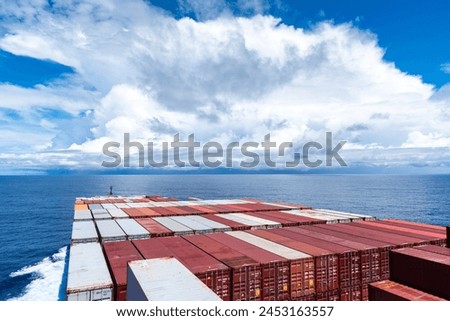View on the containers loaded on deck of the large cargo ship. She is sailing through calm, blue ocean. 