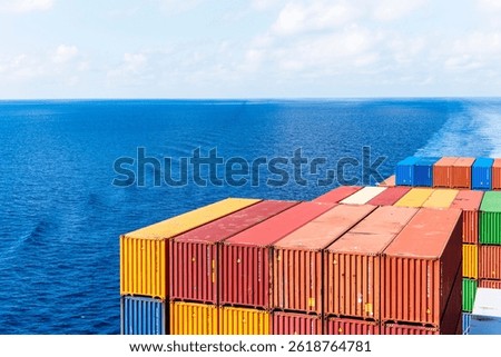 View on the containers loaded on deck of the large cargo ship. She is sailing through calm, blue ocean.